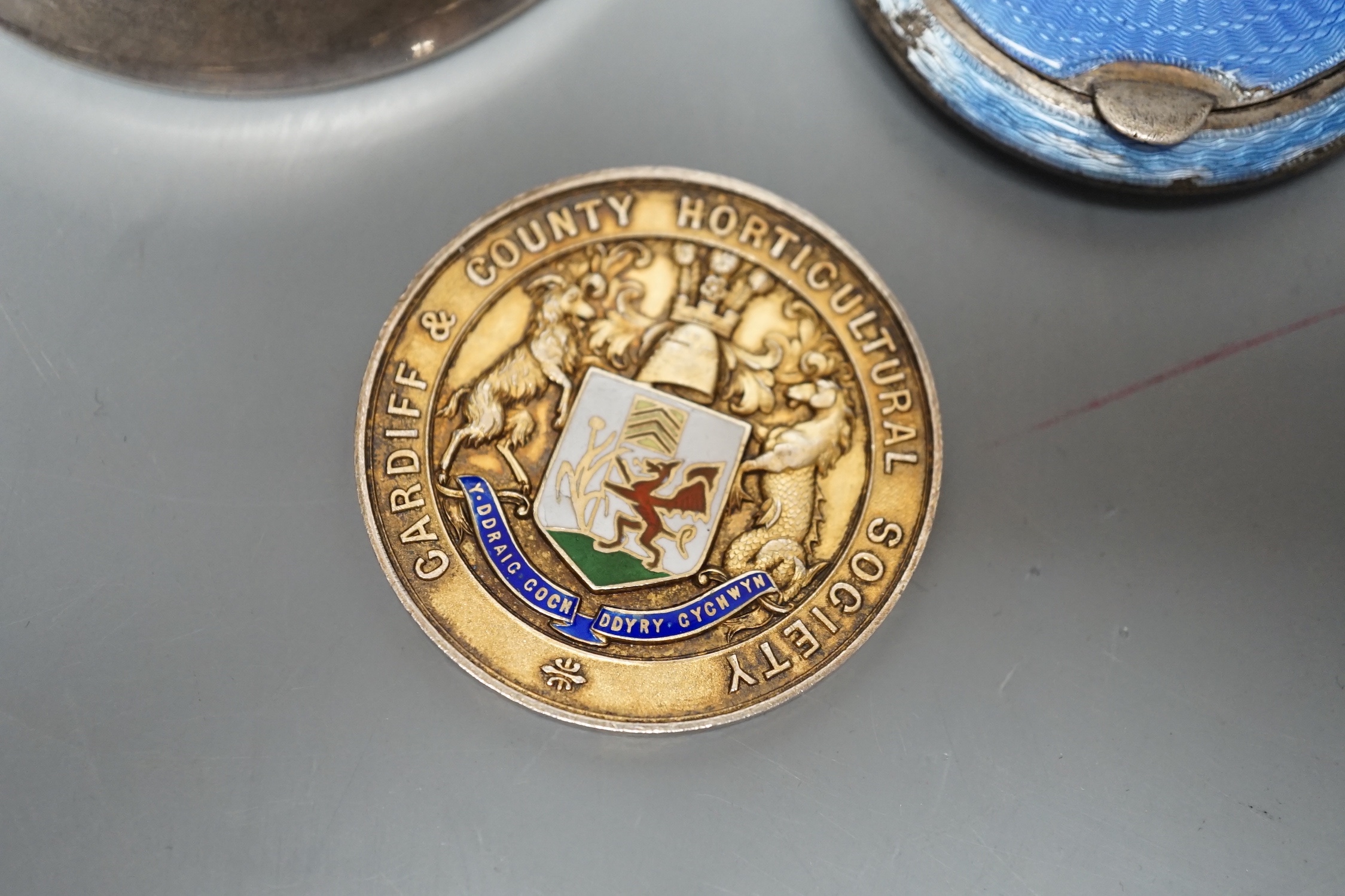 A George V silver cup holder, Birmingham, 1918, a silver and enamel Cardiff & County Horticultural Society medallion and a silver and enamel compact(a.f.)
